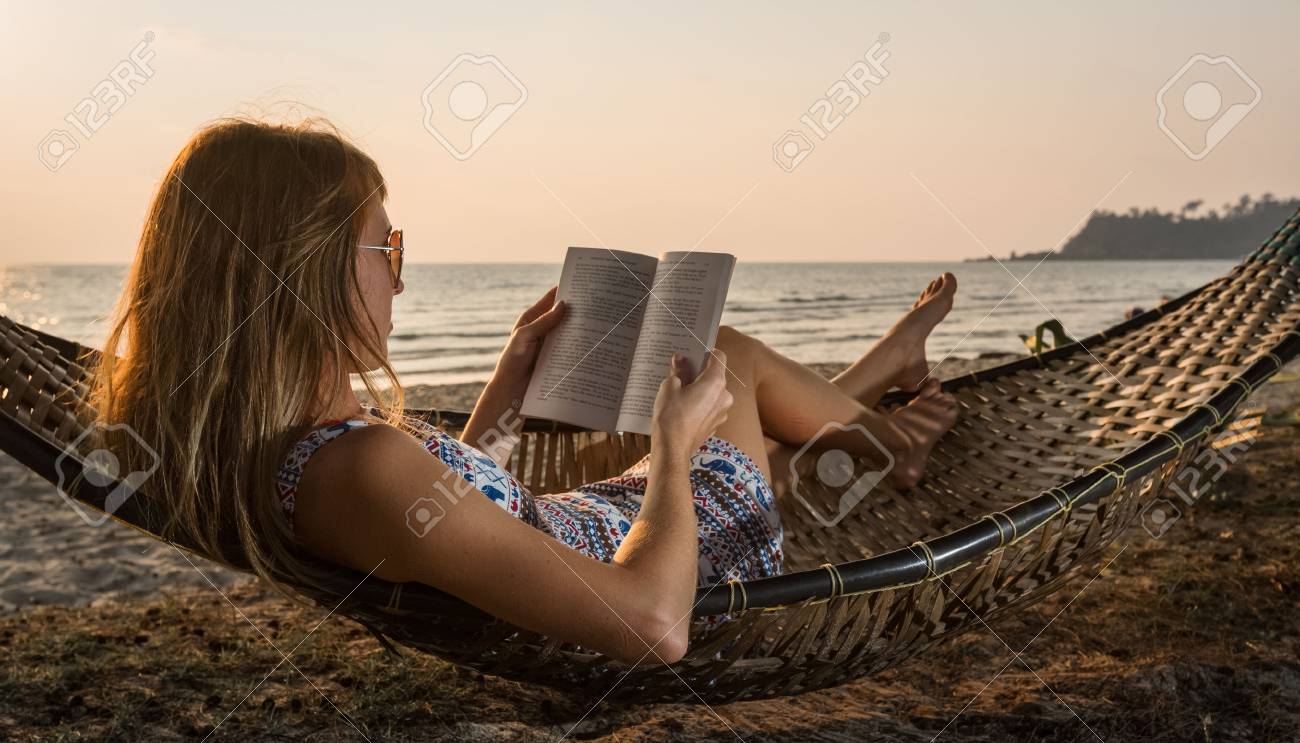 Young lady reading a book in hammock on a beach at sunset - 56103219 Young lady reading a book in hammock on a beach at sunset - 56103219