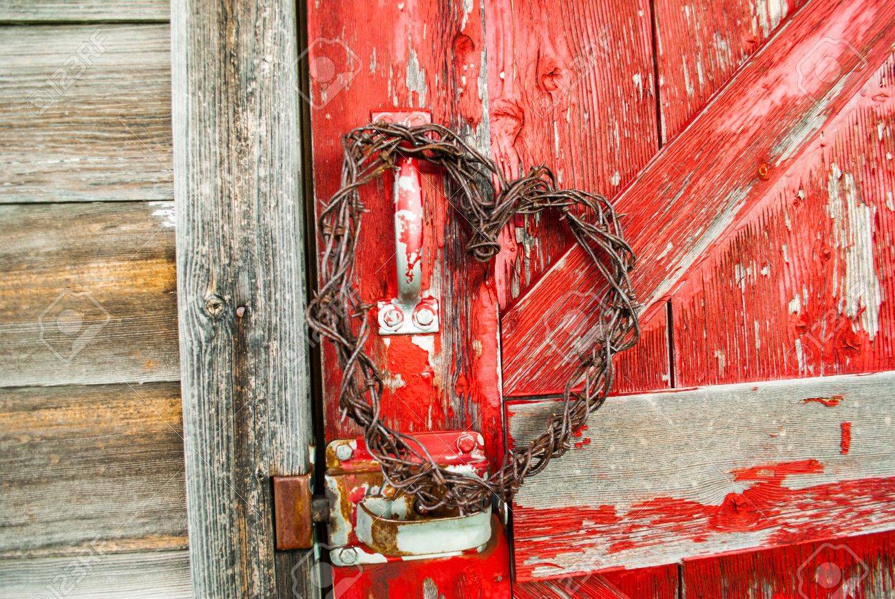 Red Barn Wood barbed wire heart hanging on old red barnwood door in sunlight Red Barn Wood barbed wire heart hanging on old red barnwood door in sunlight