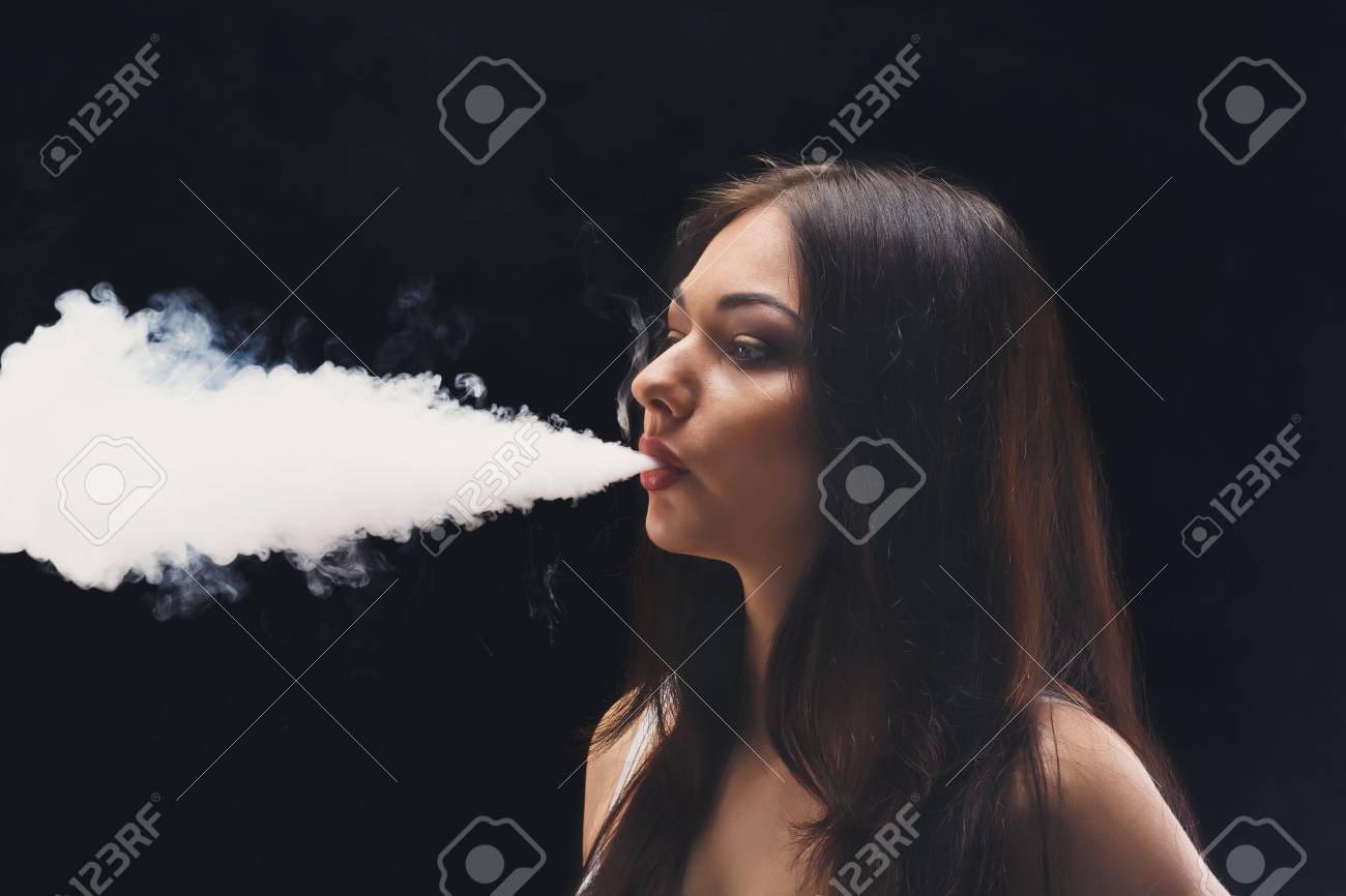 ブルネットの女性 Vaping 電子タバコ煙黒の背景のクローズ アップ 若い女性電子タバコを吸ってタバコをやめる 蒸気と代替ニコチン無料喫煙コンセプト コピー スペース の写真素材 画像素材 Image