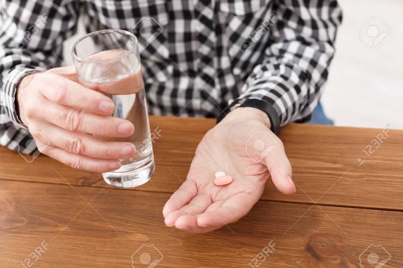 薬を飲んでる認識できない先輩の男性は 水と薬のガラスでテーブルの上に手を置きます ヘルスケア トリートメント エイジングコンセプト コピースペース の写真素材 画像素材 Image
