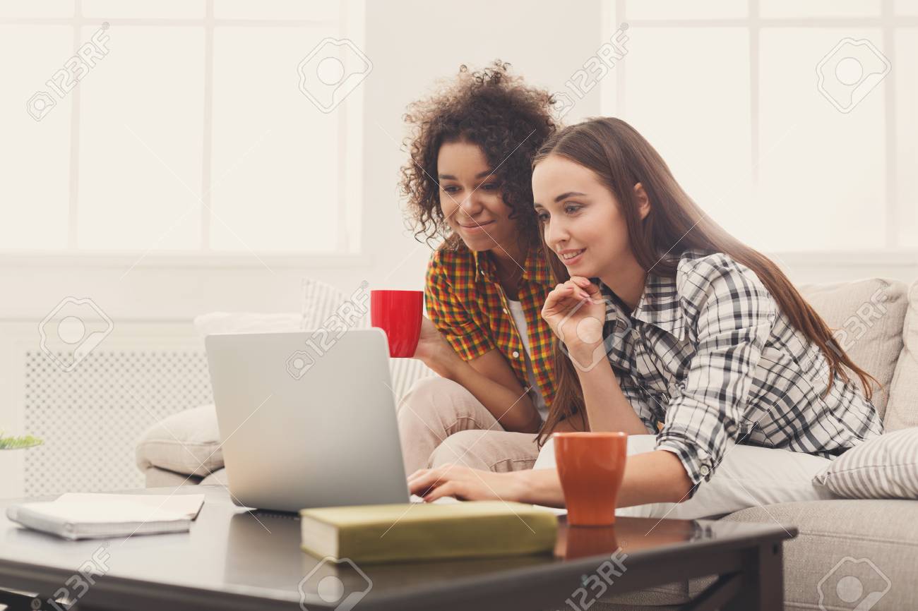 two cheerful beautiful women using laptop browsing and searching searching online