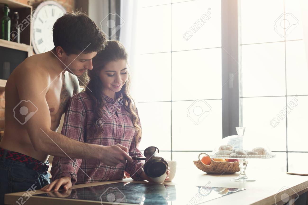 Naked Husband Is Pouring Coffee For His Wife In Loft Kitchen