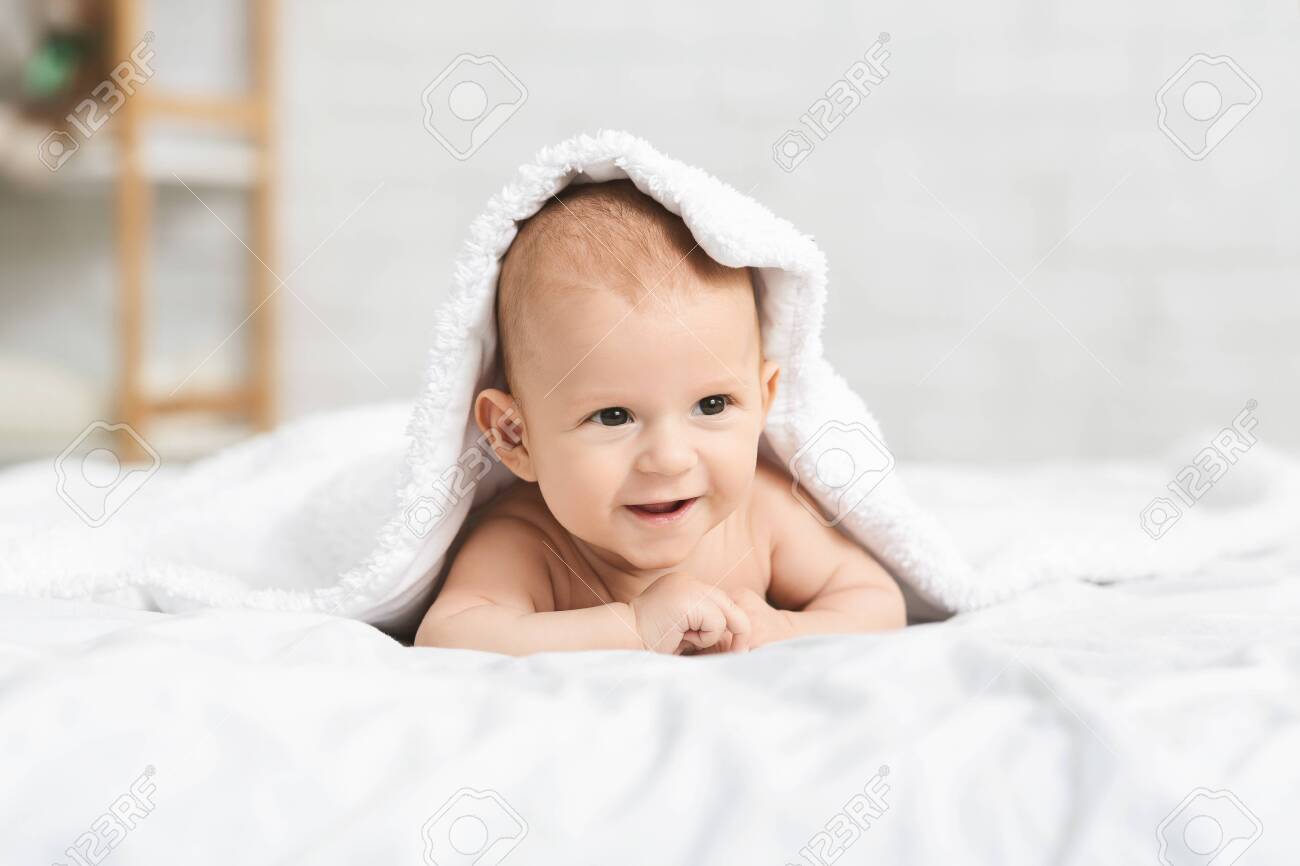 Portrait of adorable smiling baby boy lying on bed under soft white blanket, copy space - 129610041 Portrait of adorable smiling baby boy lying on bed under soft white blanket, copy space - 129610041