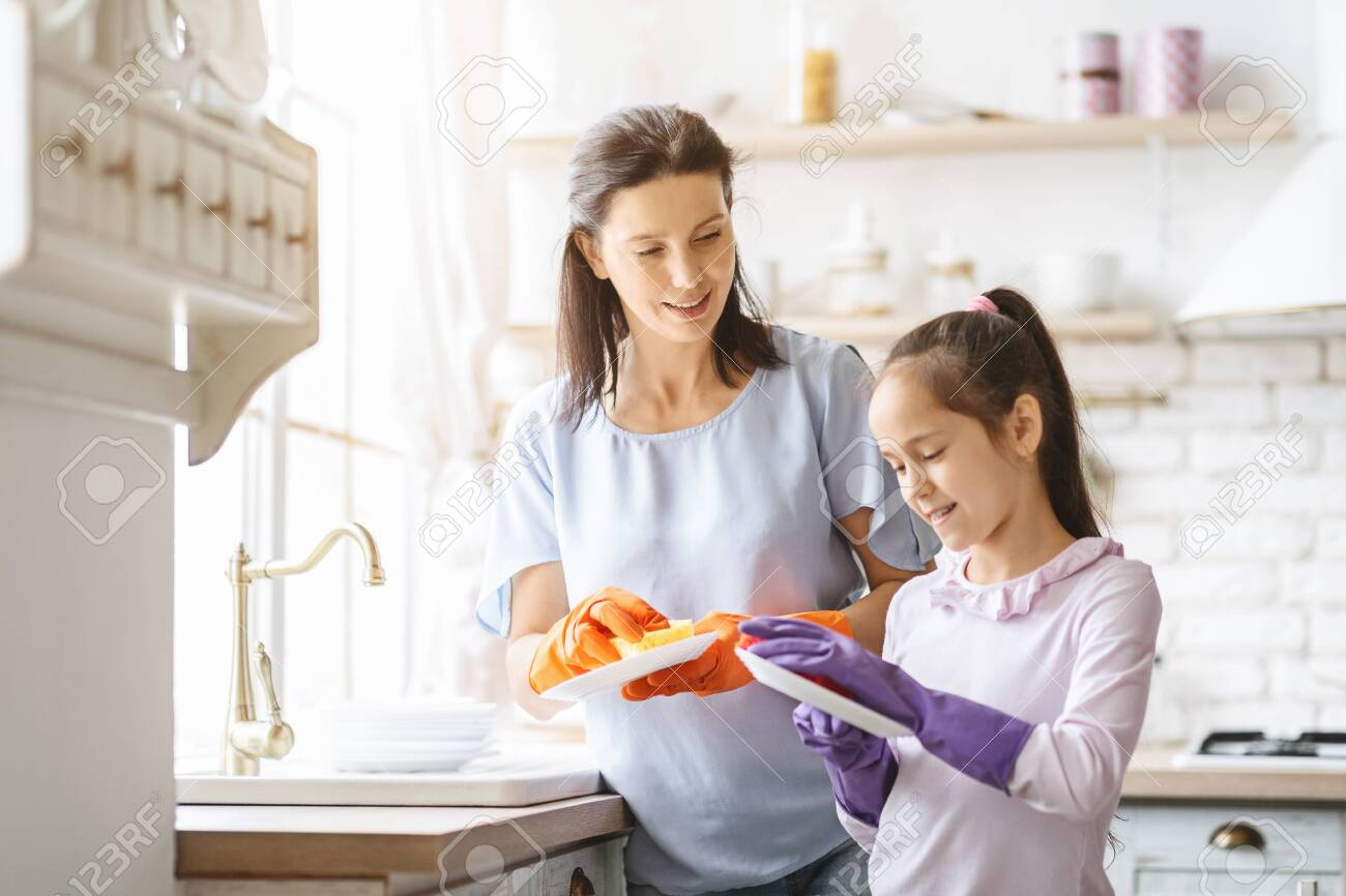 Helping hand. Cute Teenage Girl Assisting Her Mother In Washing Dishes At Family Kitchen - 130008295 Helping hand. Cute Teenage Girl Assisting Her Mother In Washing Dishes At Family Kitchen - 130008295