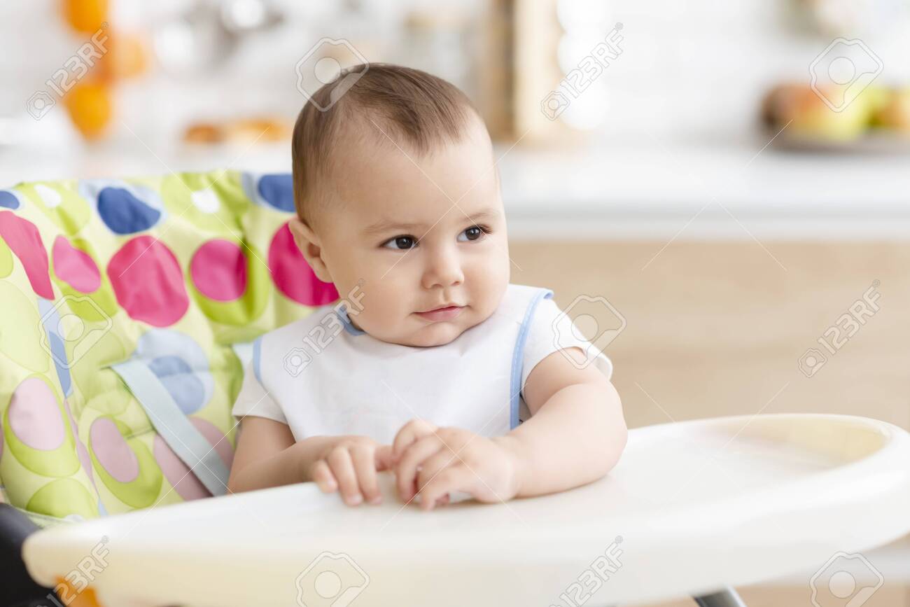 Dining time. Adorable baby sitting in high chair in kitchen , empty space - 130403698 Dining time. Adorable baby sitting in high chair in kitchen , empty space - 130403698