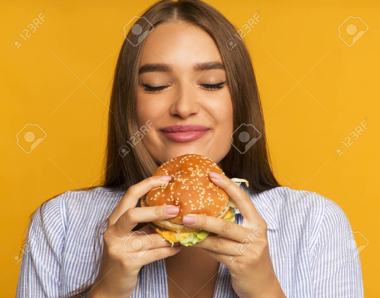 Cheat Meal. Happy Girl Eating Burger Standing Over Yellow - 131799716 Cheat Meal. Happy Girl Eating Burger Standing Over Yellow - 131799716