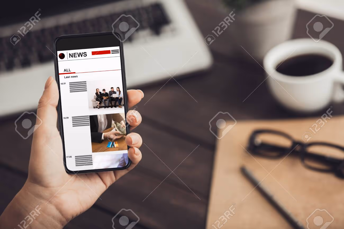 Female hand holding smartphone with last news articles on screen at table, copy space. Collage - 154886806 Female hand holding smartphone with last news articles on screen at table, copy space. Collage - 154886806