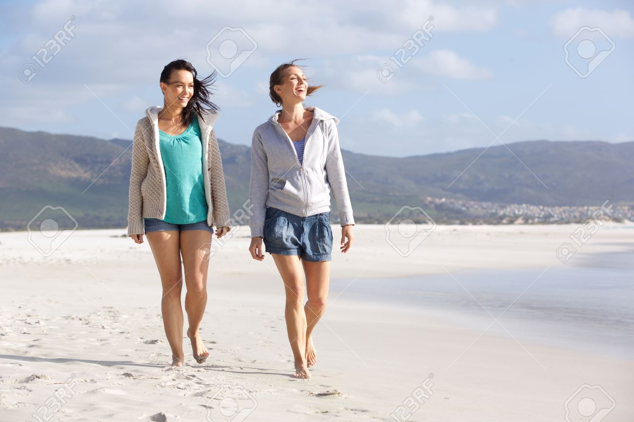 portrait of two smiling women friends walking on beach together