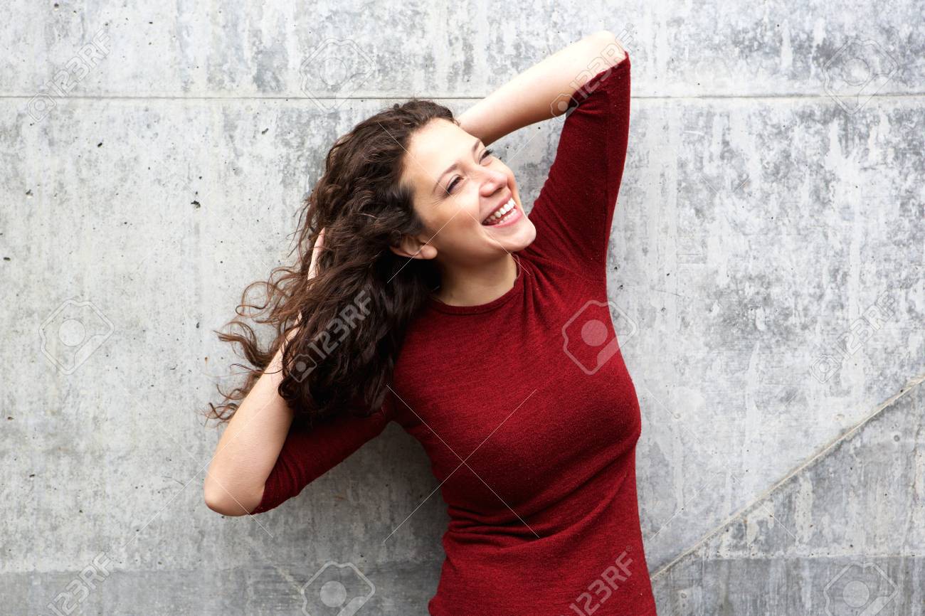 Portrait of attractive young woman laughing against gray wall - 62508423 Portrait of attractive young woman laughing against gray wall - 62508423