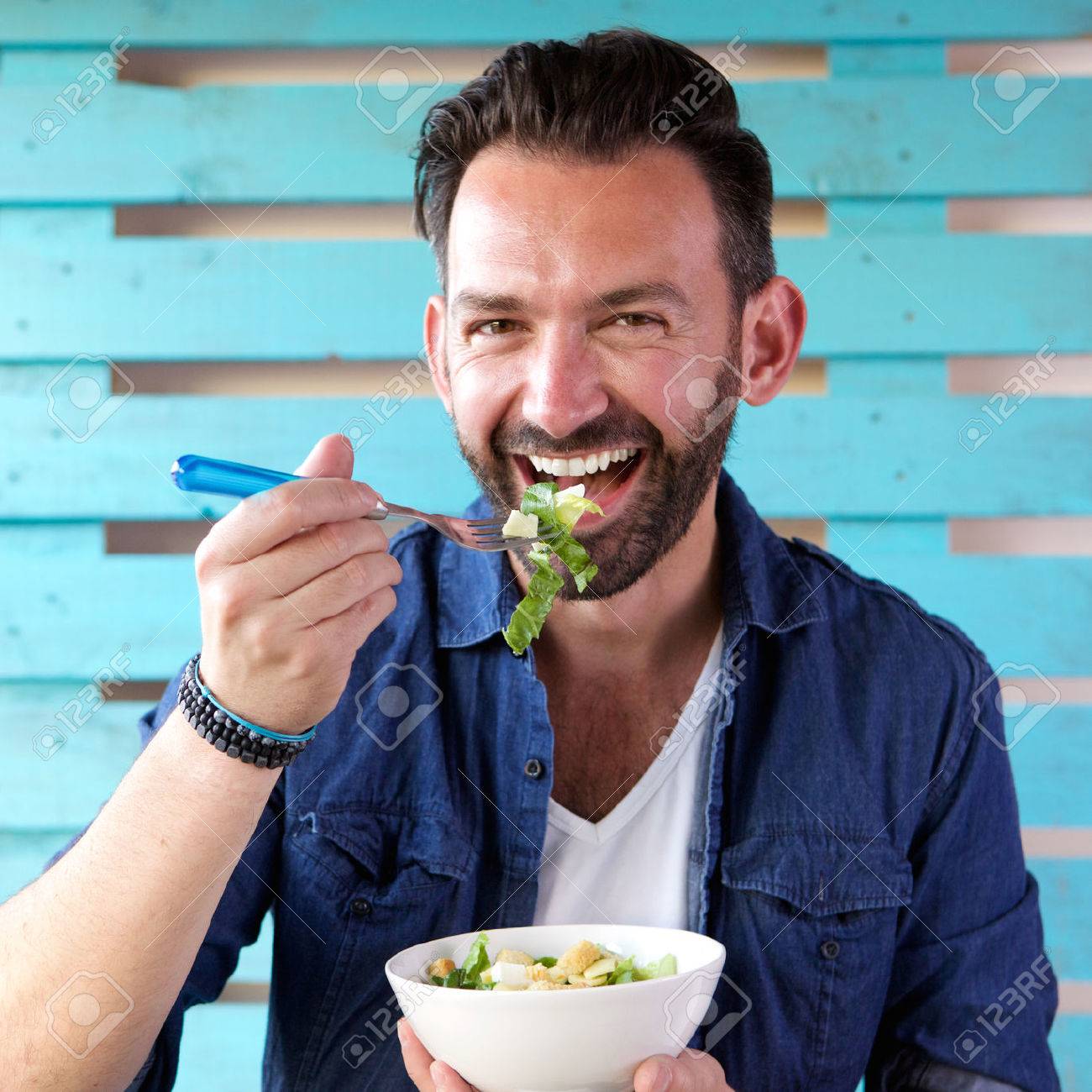 Close up portrait of cheerful man eating salad from bowl - 63536620 Close up portrait of cheerful man eating salad from bowl - 63536620