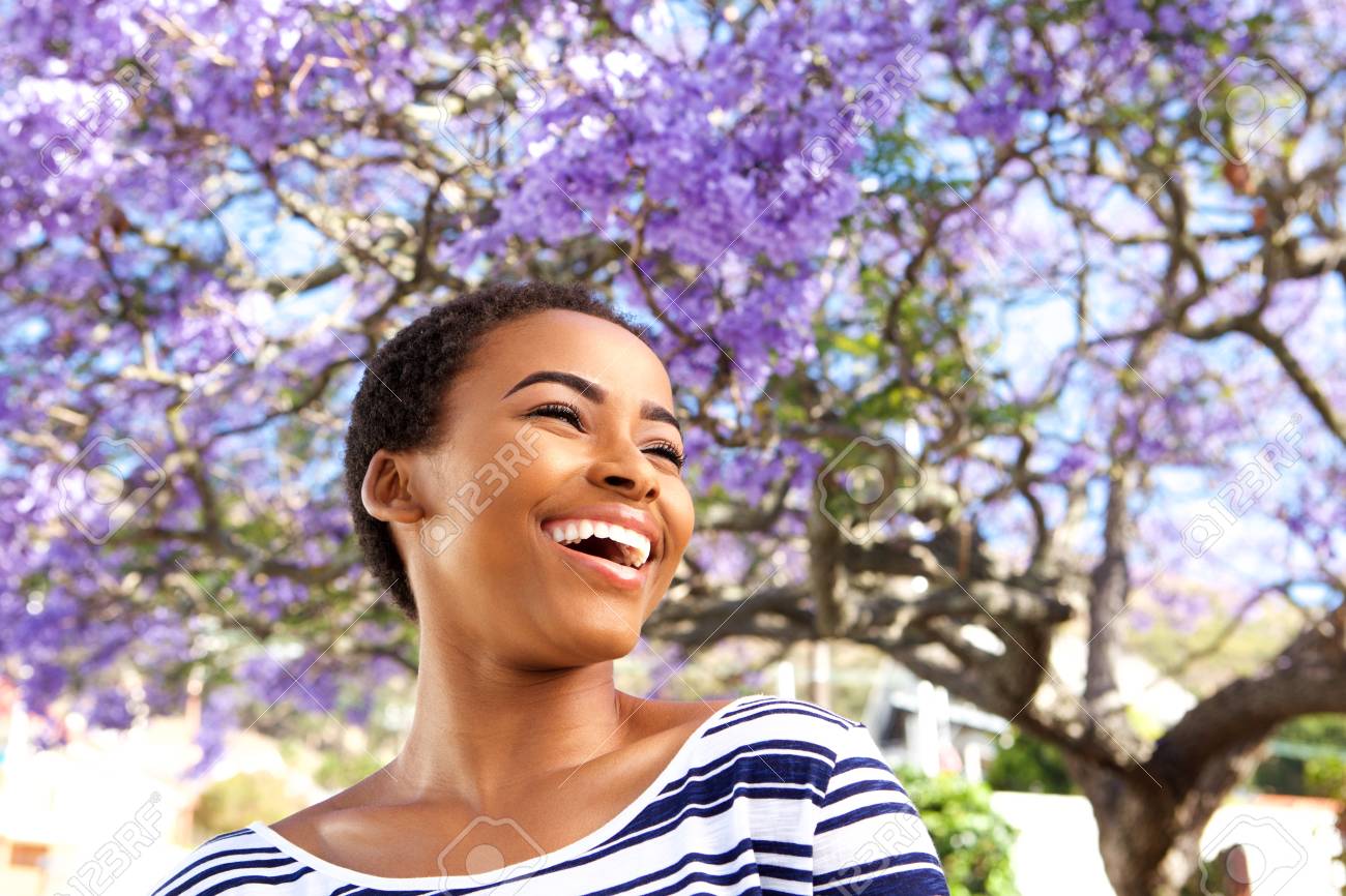 Portrait of attractive young black woman laughing outdoors by flower tree - 71517809 Portrait of attractive young black woman laughing outdoors by flower tree - 71517809
