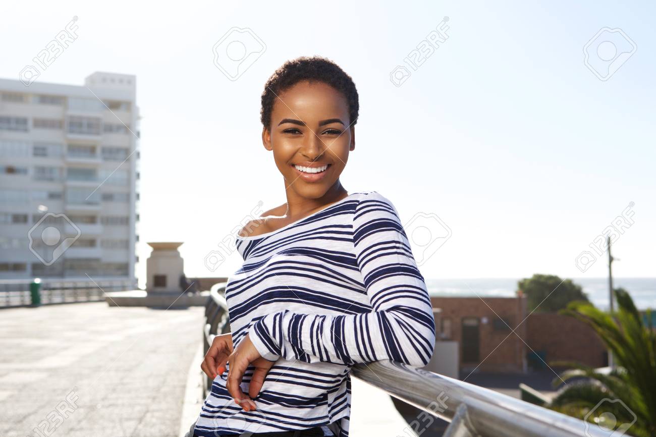 Side portrait of smiling young black woman standing outside in summer - 71517854 Side portrait of smiling young black woman standing outside in summer - 71517854