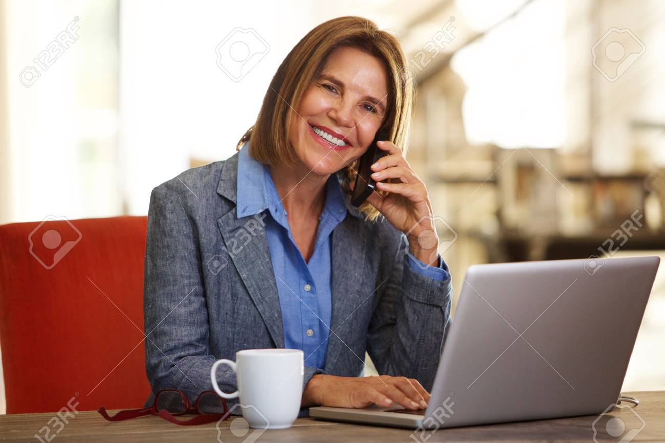 Portrait of smiling business woman sitting at desk with phone and laptop - 72425447 Portrait of smiling business woman sitting at desk with phone and laptop - 72425447