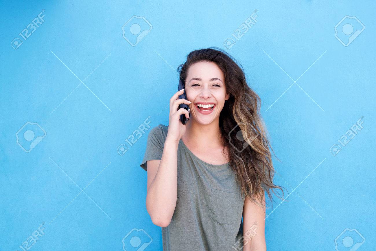 Front portrait of young laughing woman talking on cellphone against blue background - 72711326 Front portrait of young laughing woman talking on cellphone against blue background - 72711326