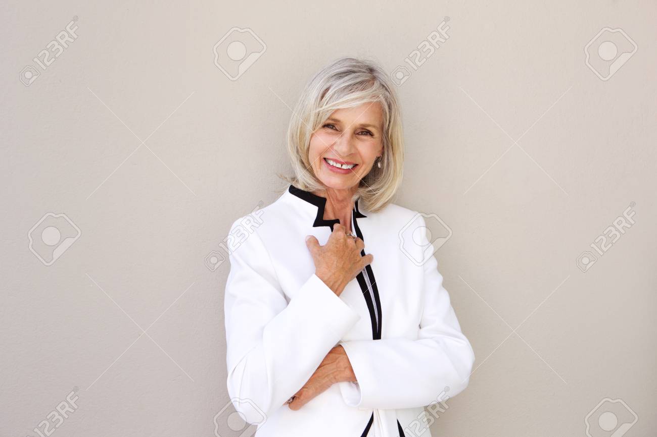 Portrait of beautiful older woman smiling and standing by wall - 74022112 Portrait of beautiful older woman smiling and standing by wall - 74022112
