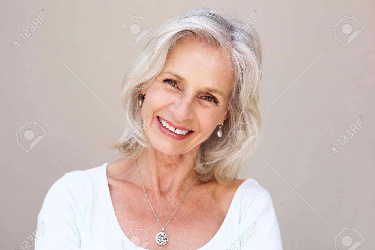 Close up portrait of beautiful older woman smiling and standing by wall - 74021919 Close up portrait of beautiful older woman smiling and standing by wall - 74021919