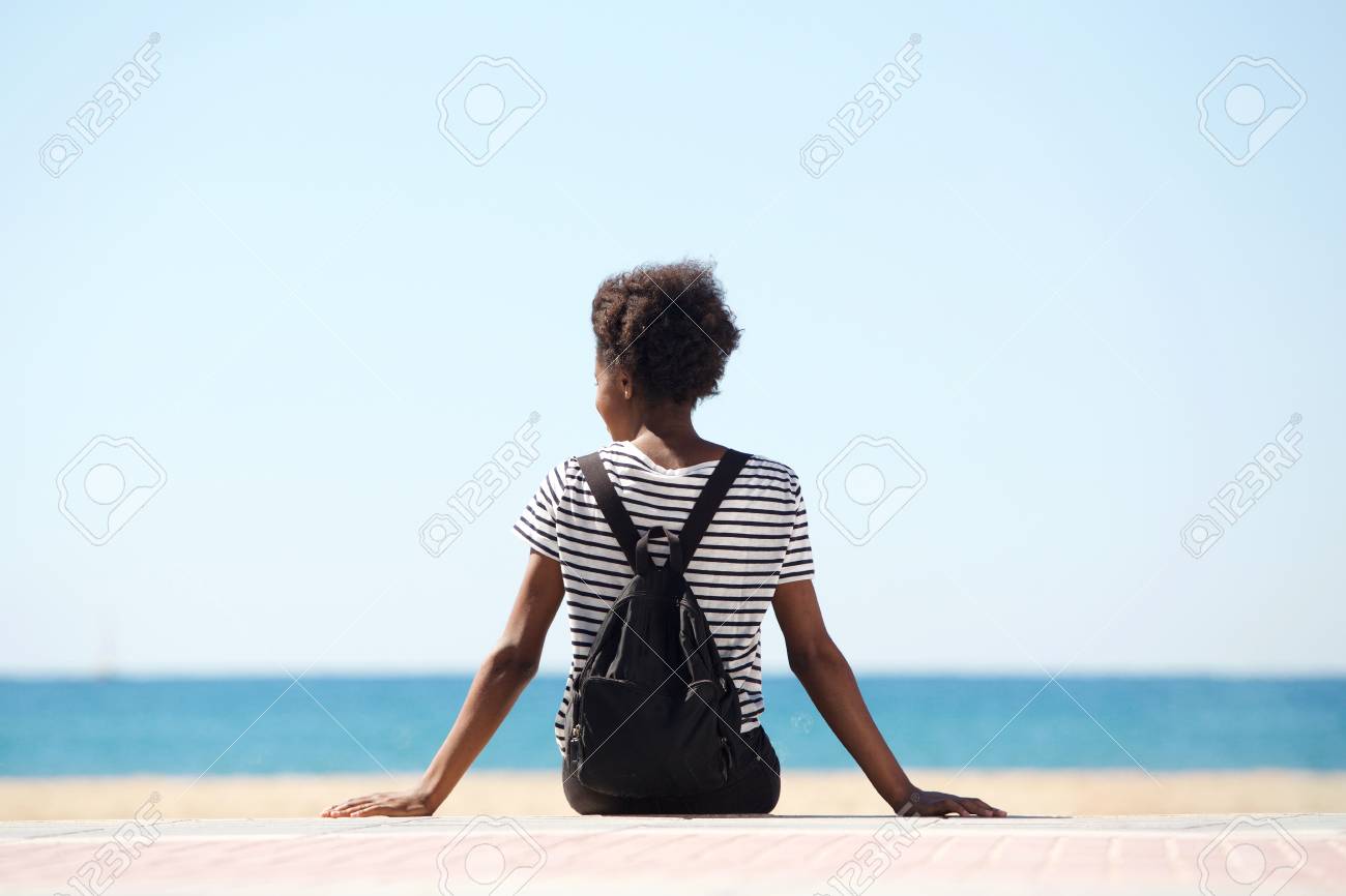 Rear view portrait of young woman sitting by the beach on summer day - 81319700 Rear view portrait of young woman sitting by the beach on summer day - 81319700