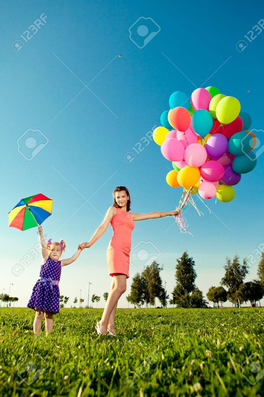 Niña Hermosa La Madre De Color Globos Y Paraguas Del Arco Iris Que Sostienen En El Niño Y La Madre En Un Campo Con Flores. Kid Con El Descanso