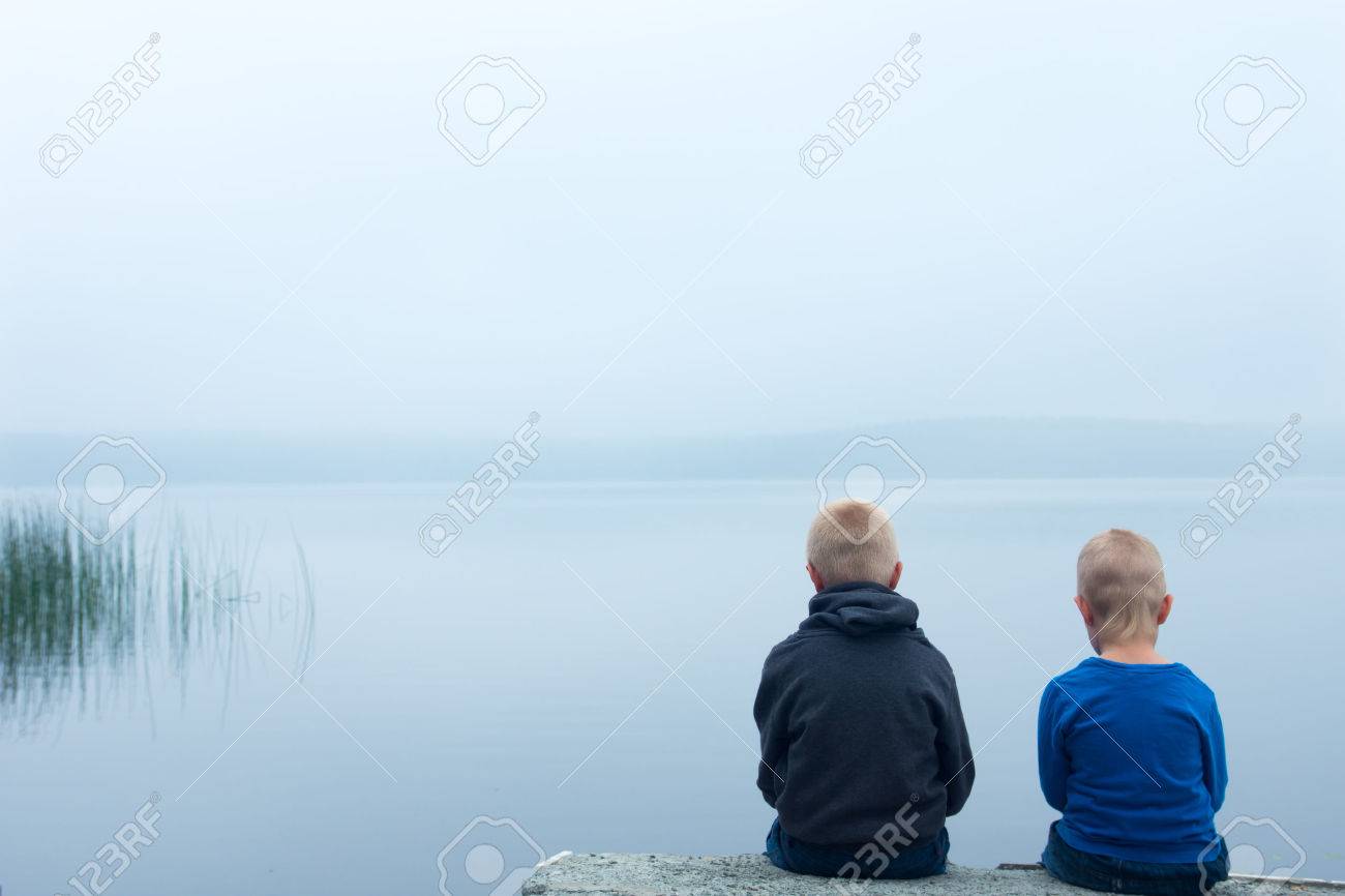 two sad children boys brothers sitting alone by lake in a stock