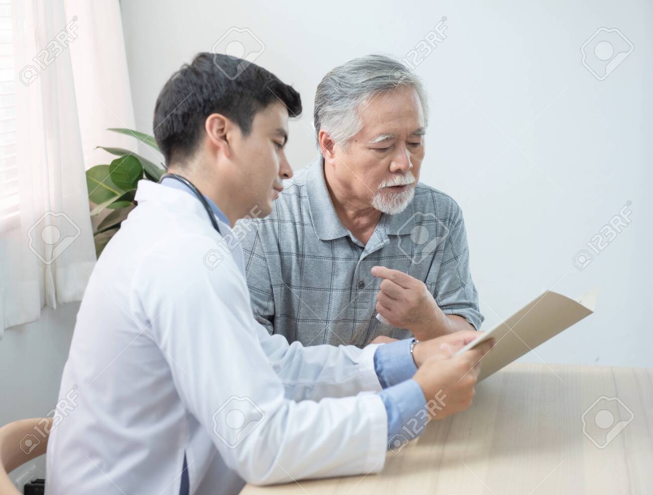 Young caucasian doctor read and explaining consult medical test document for asian elder senior man while visit patient at home.healthcare and medical concept. - 143763636 Young caucasian doctor read and explaining consult medical test document for asian elder senior man while visit patient at home.healthcare and medical concept. - 143763636