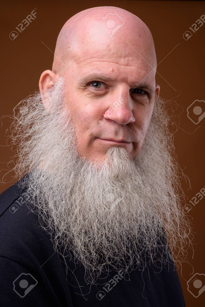 Mature Bald Man With Long Gray Beard Against Brown Background