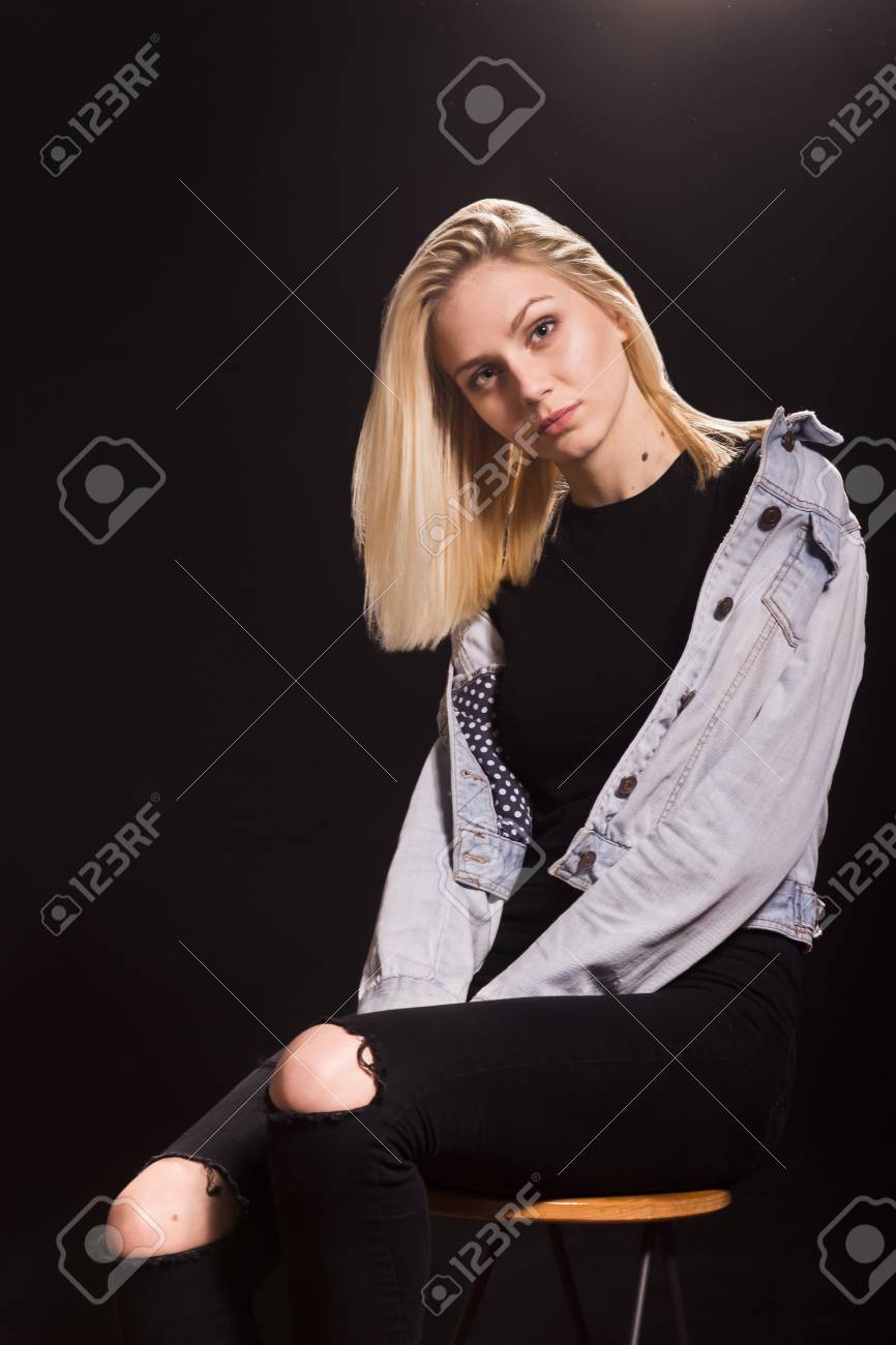 両性具有アダルト少女 19 の女性ファッション モデル ポーズ。黒のジーンズ、黒の T シャツ、デニム ジャケット  カジュアルな服を着て座っています。スタジオ黒背景。の写真素材・画像素材 Image 74409322