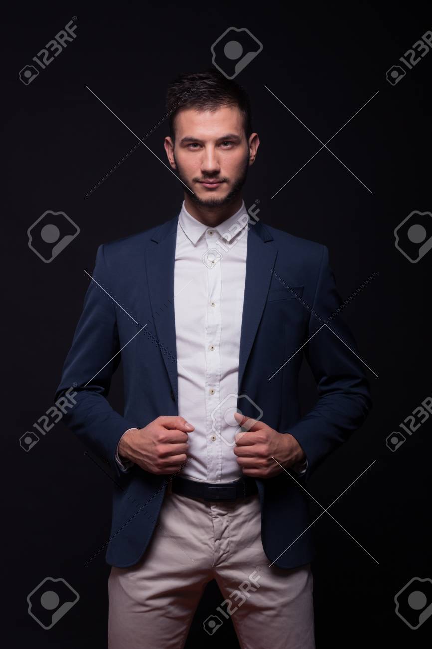 Adulto joven modelo de hombre elegante camisa pantalones de traje, la celebración de la chaqueta azul, fondo negro Adulto joven modelo de hombre elegante camisa pantalones de traje, la celebración de la chaqueta azul, fondo negro