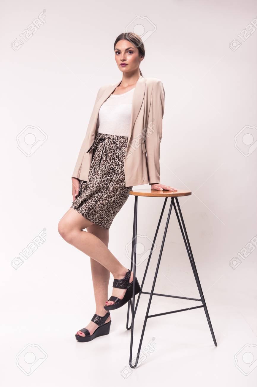 一人の若い白人女性 代 29 歳 ファッションのモデル スタジオ 白い背景 高いヒールの靴 おしゃれな シャツ スカート ブレザー ポーズ バースツール の写真素材 画像素材 Image