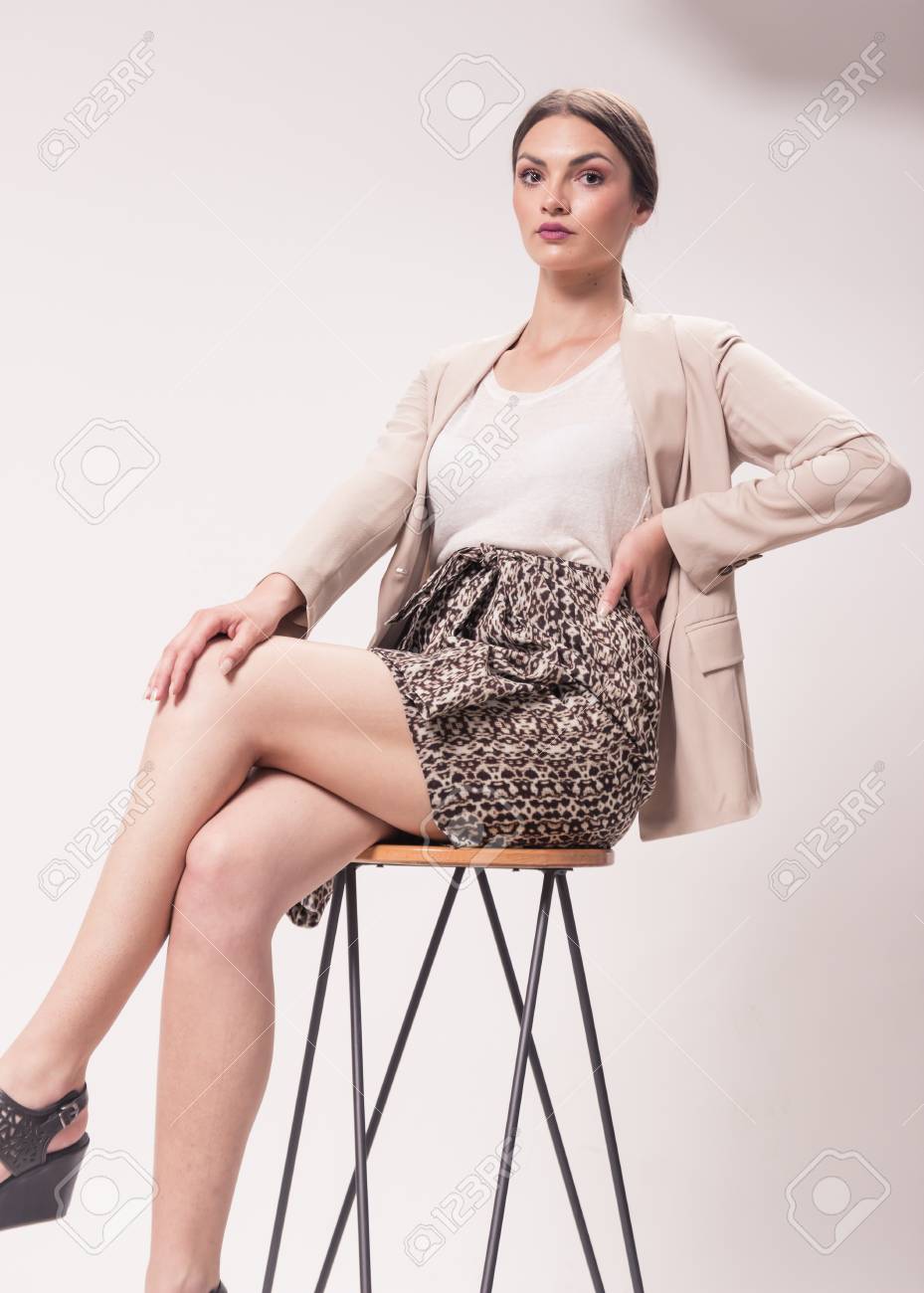 一人の若い白人女性 代 29 歳 ファッション モデル スタジオ 白い背景 高いヒールの靴 おしゃれな シャツ スカート ブレザー バーのスツールに座って の写真素材 画像素材 Image