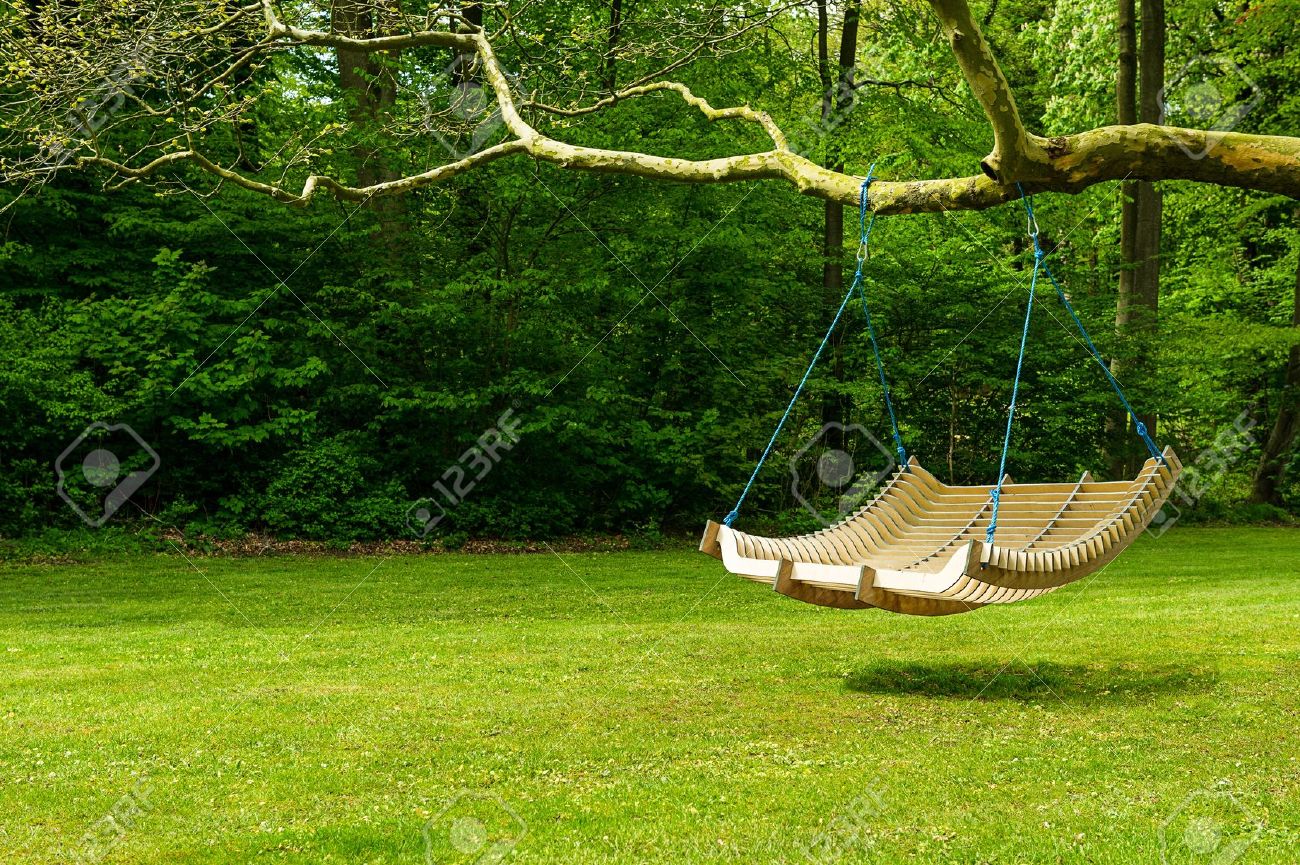 Curved swing bench hanging from the bough of a tree in a lush garden with woodland backdrop for relaxing on those hot summer days - 15183530 Curved swing bench hanging from the bough of a tree in a lush garden with woodland backdrop for relaxing on those hot summer days - 15183530