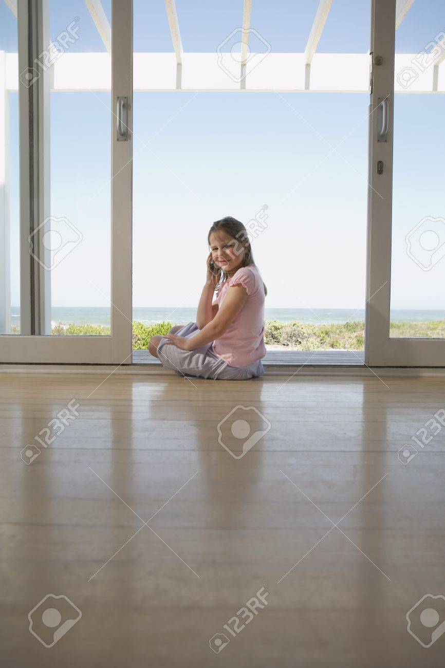 Girl Using Mobile Phone Sitting On Floor In Doorway Stock Photo
