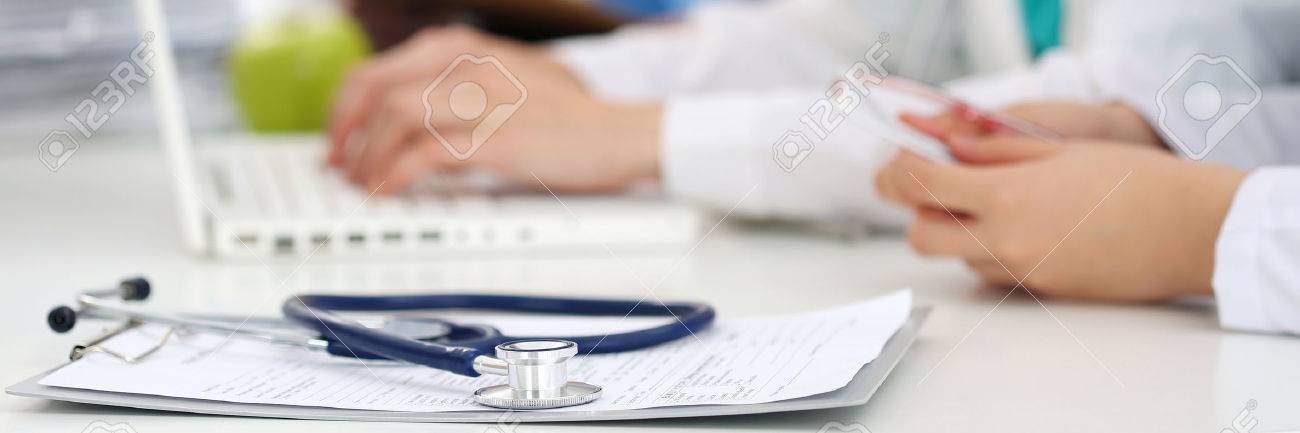 Medicine doctor's working table. Focus on stethoscope. Two female medicine doctors operating on background. Healthcare and medical conceptBottle of pills and stethoscope laying on clipping board with prescription blank. Medicine doctor's working table. He - 51481553 Medicine doctor's working table. Focus on stethoscope. Two female medicine doctors operating on background. Healthcare and medical conceptBottle of pills and stethoscope laying on clipping board with prescription blank. Medicine doctor's working table. He - 51481553
