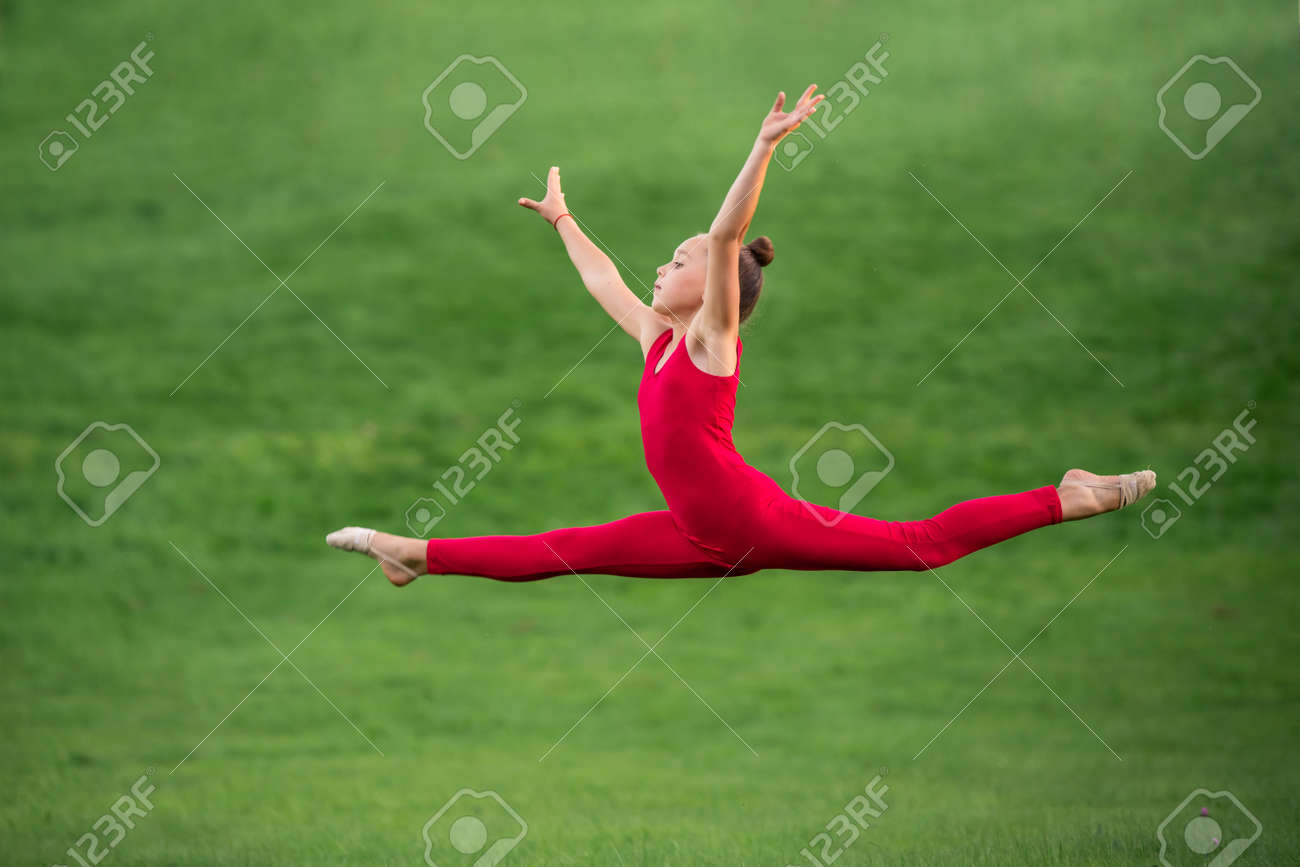 女子高生 レオタード  真っ赤なオーバーオールを着た女子高生が公園の芝生で体操をし、スプリットジャンプで飛ぶの写真素材・画像素材 Image 167275075