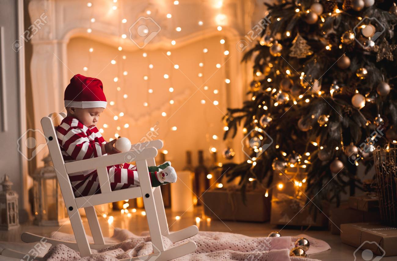 Luci Di Natale In Camera.Immagini Stock Bambino 1 Anno Di Eta Che Indossa La Tuta Di Babbo Natale Seduto Sulla Sedia A Dondolo Con L Albero Di Natale E Luci Su Sfondo In Camera Buon Natale