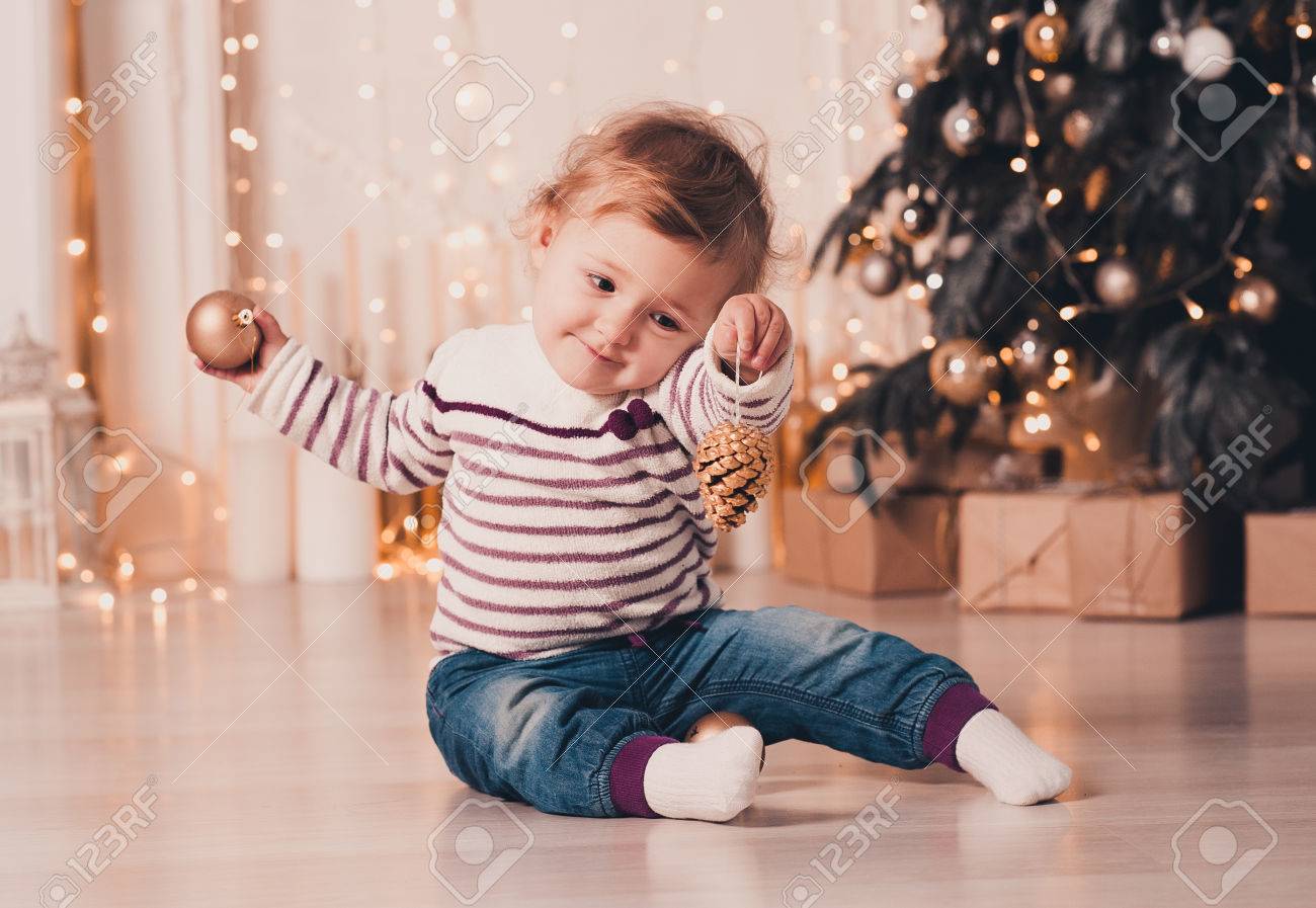 Smiling Baby Girl Under 1 Year Old Playing With Christmas Ball Over Christmas Tree In Room Sitting On Floor Wearing Stylish Knitted Sweater Celebration Holiday Season Stock Photo Picture And Royalty Free