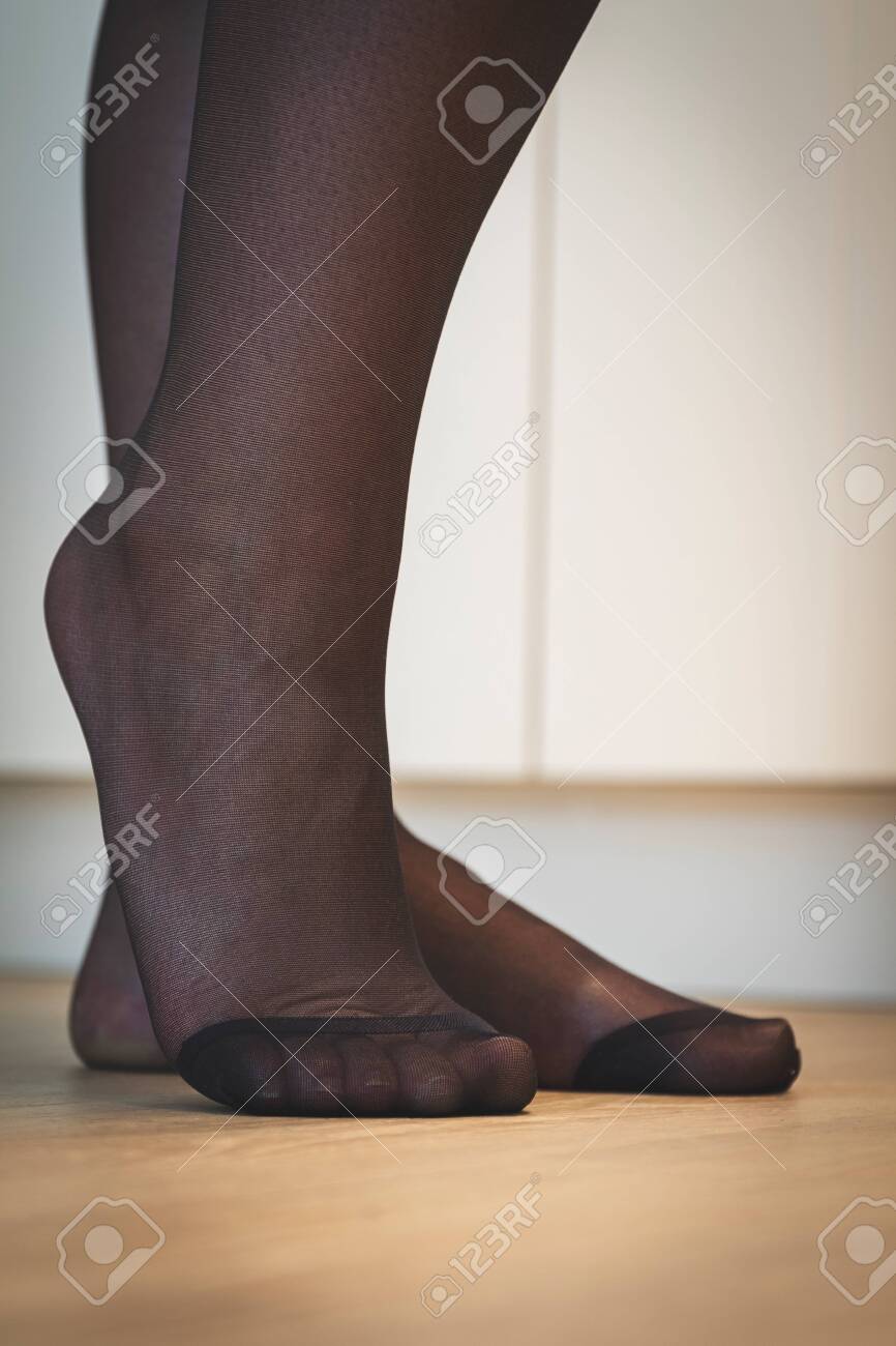 A Close Up Portrait Of The Elegant Feet Of A Girl In Black Pantyhose With  The Nylon At The Toes Being Reinforced Standing On A Wooden Floor And  Posing. Stock Photo, Picture