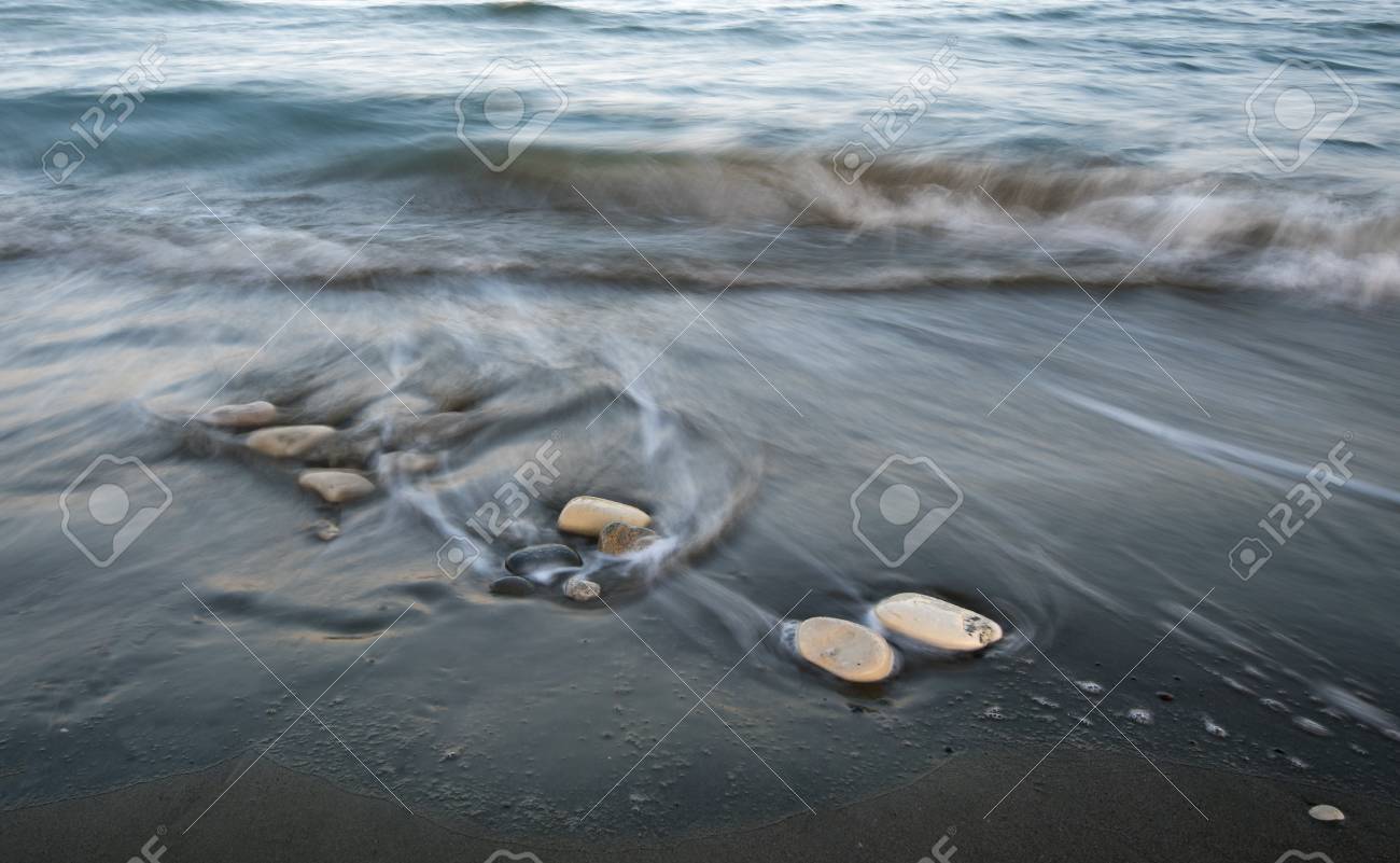 pebbles on the beach on a black sand and flowing sea water creating