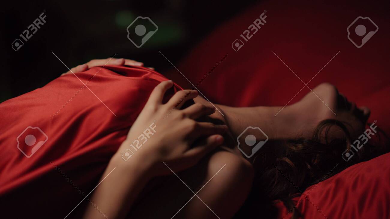 Woman touching her body passionately under red silk sheet erotic intense craving