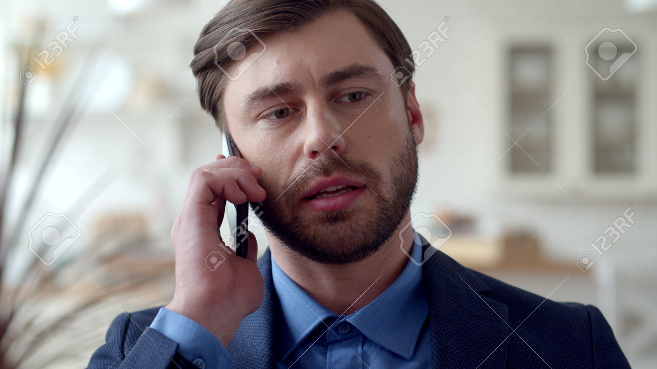 Closeup attractive business man making phone call at home. Portrait of focused guy talking on cellphone at remote office. Serious male freelancer speaking by phone at modern house. - 162271287 Closeup attractive business man making phone call at home. Portrait of focused guy talking on cellphone at remote office. Serious male freelancer speaking by phone at modern house. - 162271287