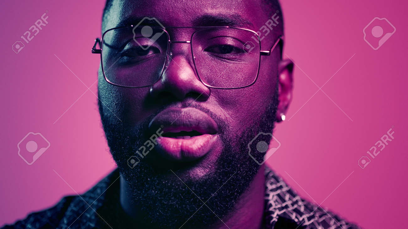 Closeup fancy afro guy staring at lenses indoors. Portrait of romantic male person flirting on pink background. African american guy sending kisses in studio. - 159609815 Closeup fancy afro guy staring at lenses indoors. Portrait of romantic male person flirting on pink background. African american guy sending kisses in studio. - 159609815