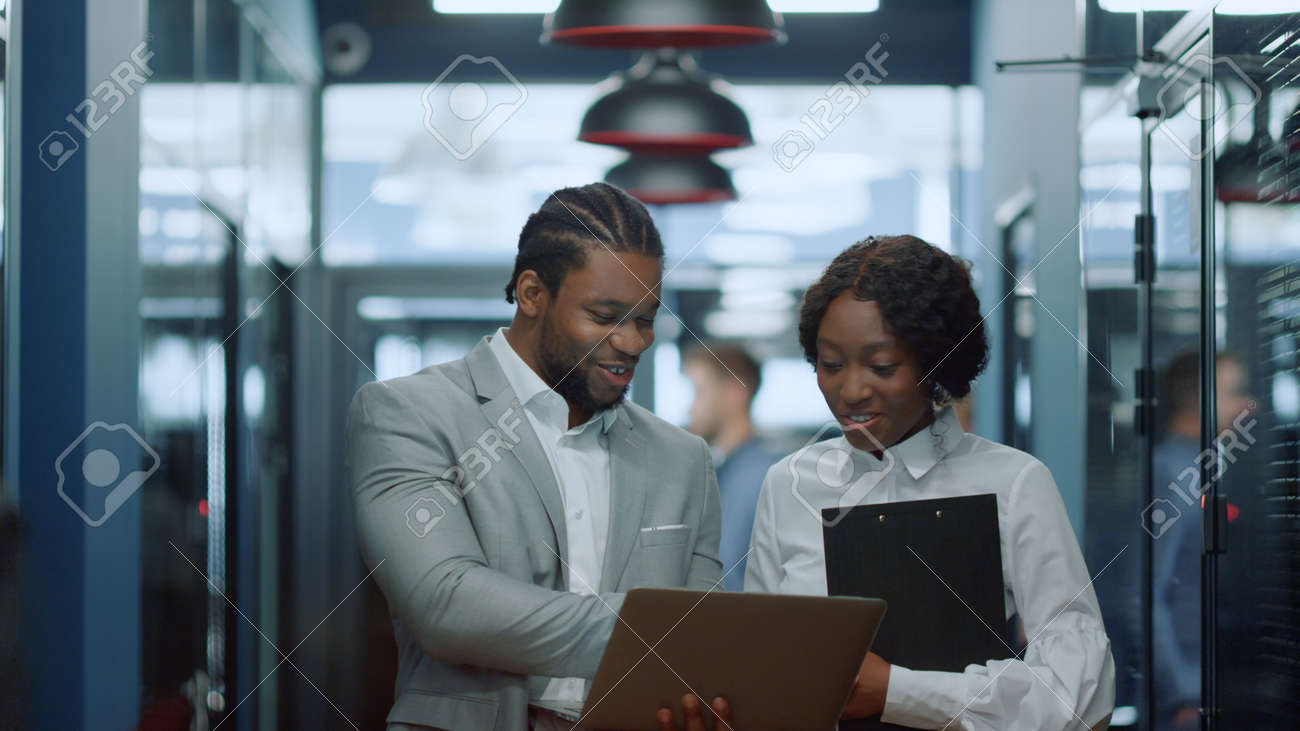 Portrait of smiling african business people using laptop in corridor. African american colleagues working in business center hallway. Cheerful afro couple discussing project in office interior - 158485720 Portrait of smiling african business people using laptop in corridor. African american colleagues working in business center hallway. Cheerful afro couple discussing project in office interior - 158485720