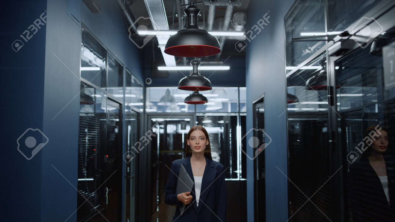 Portrait of smiling businesswoman posing in office corridor. Closeup charming female manager looking at camera in office hallway. Positive business woman holding folder in business center interior. - 158542023 Portrait of smiling businesswoman posing in office corridor. Closeup charming female manager looking at camera in office hallway. Positive business woman holding folder in business center interior. - 158542023