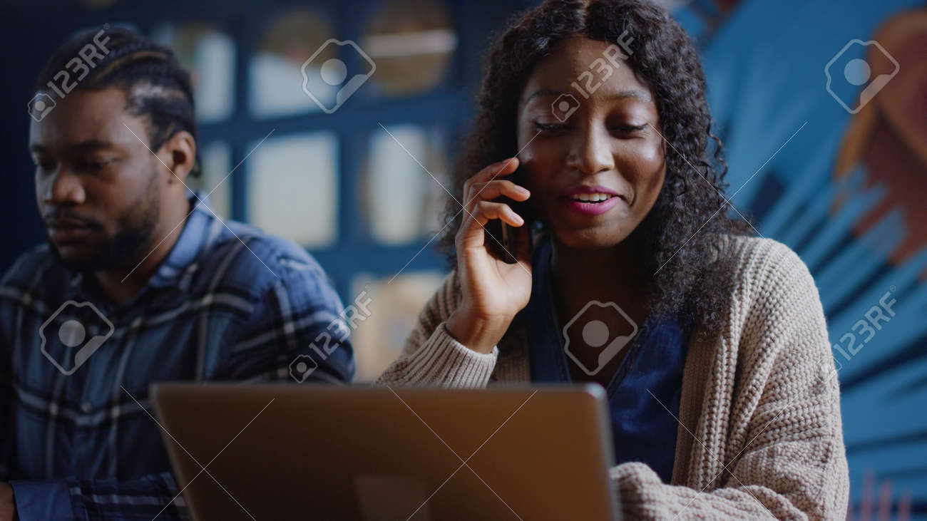 Closeup african american colleagues working at workplace in business center. Positive afro business woman talking phone in office. Portrait of smiling girl calling phone in creative coworking. - 158542089 Closeup african american colleagues working at workplace in business center. Positive afro business woman talking phone in office. Portrait of smiling girl calling phone in creative coworking. - 158542089