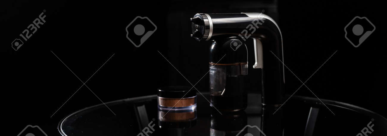 A close-up of the instant tanning equipment. Gun spraying paint for leather and matting body powder on a black background - 170497164 A close-up of the instant tanning equipment. Gun spraying paint for leather and matting body powder on a black background - 170497164