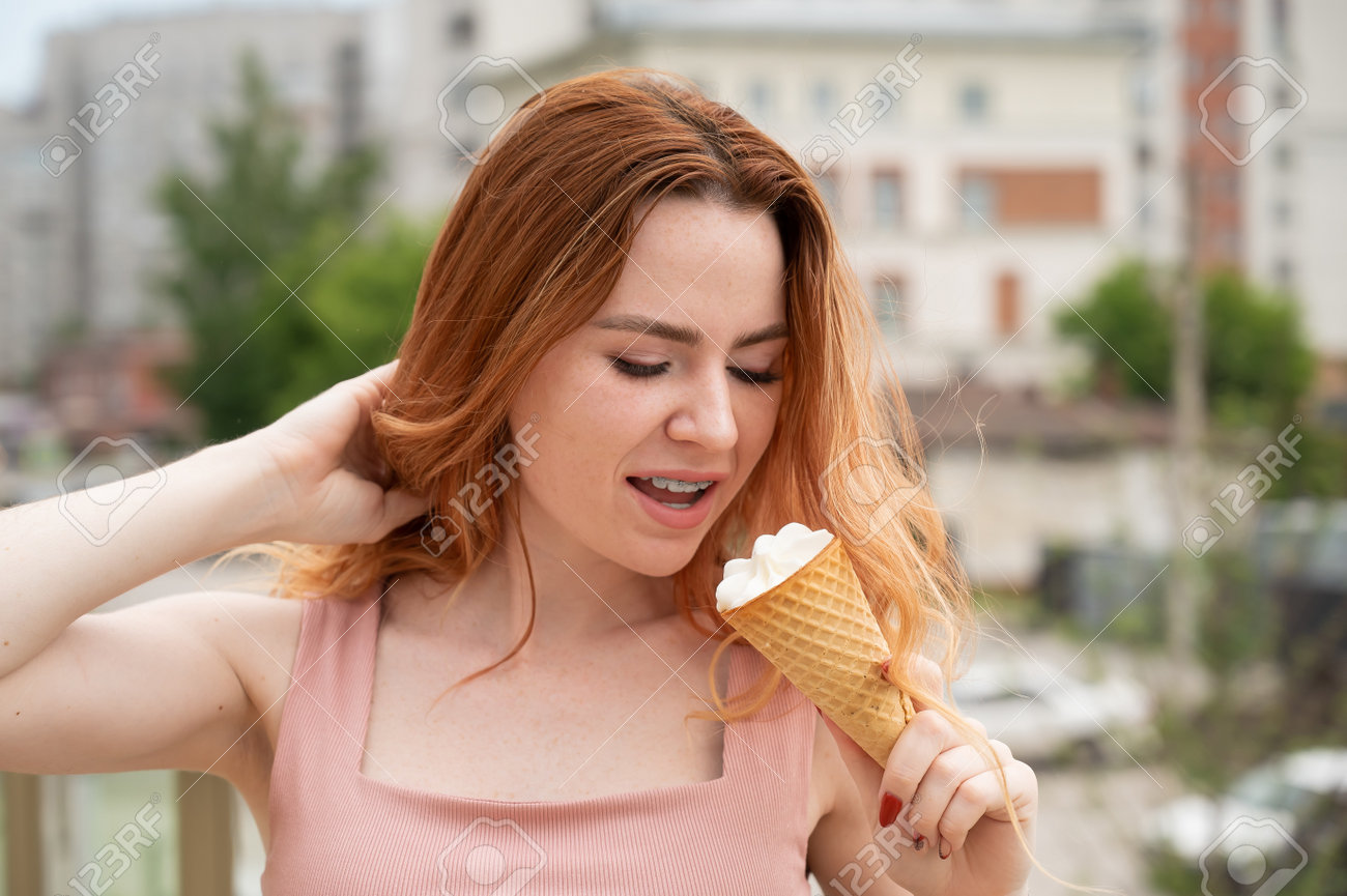 Portrait of young beautiful red-haired woman smiling with braces and going to eat ice cream cone outdoors in summer - 171679517 Portrait of young beautiful red-haired woman smiling with braces and going to eat ice cream cone outdoors in summer - 171679517