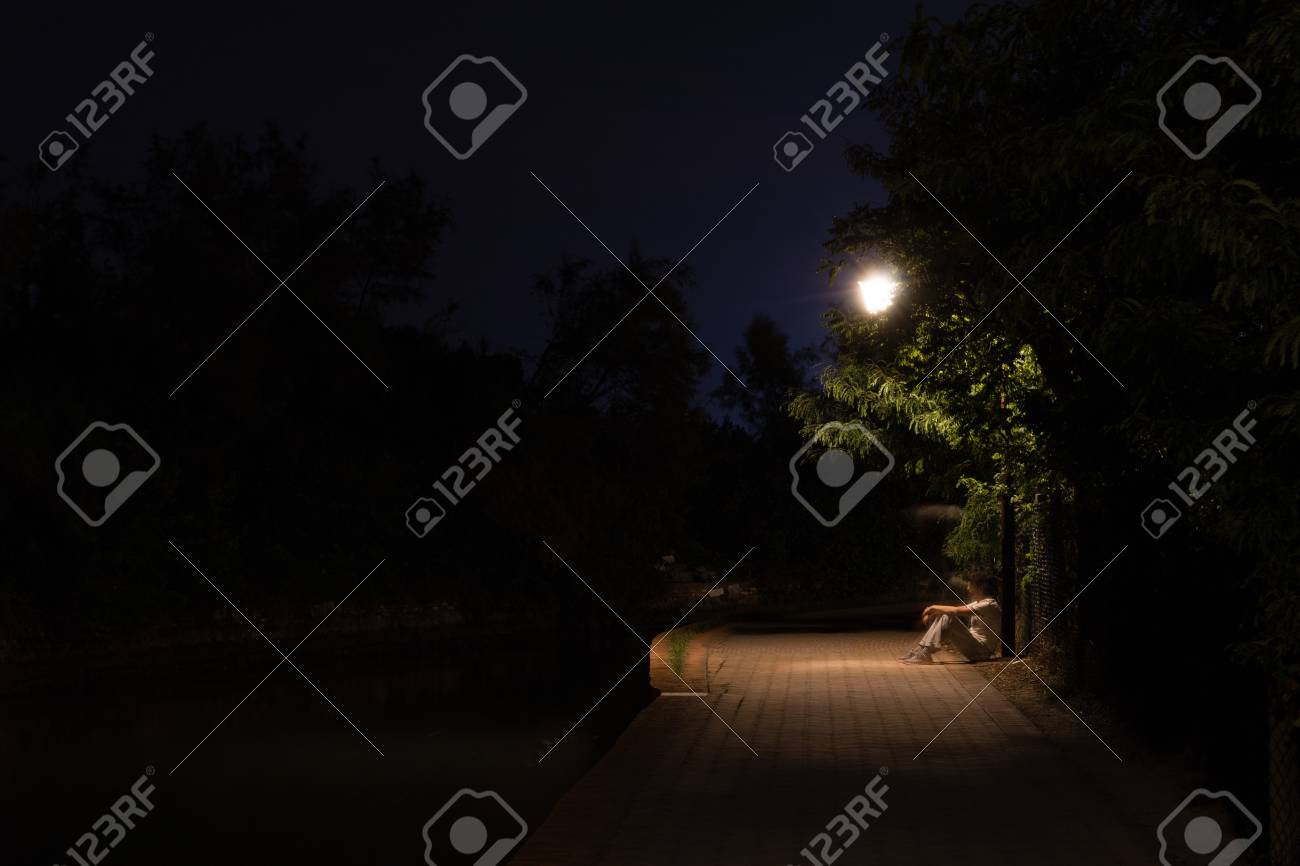 夜　公園　露出 街灯の下の暗い通りに座っている人の二重露出の夜のシーン。公園の道路上の後退男性のシルエット。街の川沿いを進む動きのぼやけの人間の姿。長いシャッター。の写真素材・画像素材  Image 97715253