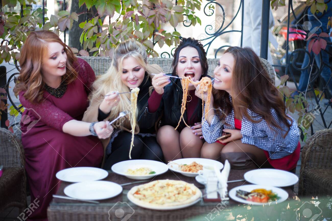 Four young women having lunch in a cafe. Pasta in a summer cafe. - 130224764 Four young women having lunch in a cafe. Pasta in a summer cafe. - 130224764