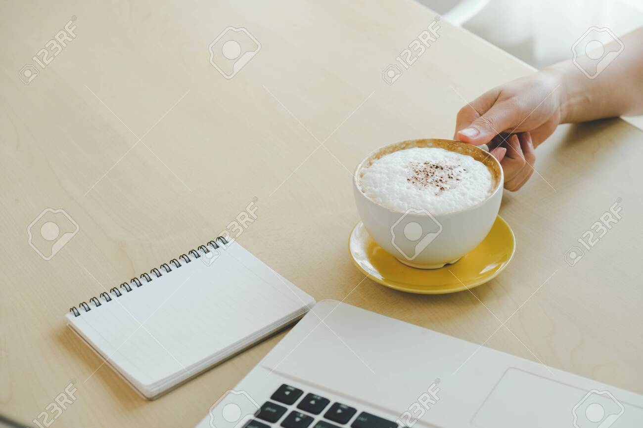 Closeup image of woman hand holding a cup of hot coffee on wooden table, working with computer laptop, freelance and work concept - 122663069 Closeup image of woman hand holding a cup of hot coffee on wooden table, working with computer laptop, freelance and work concept - 122663069
