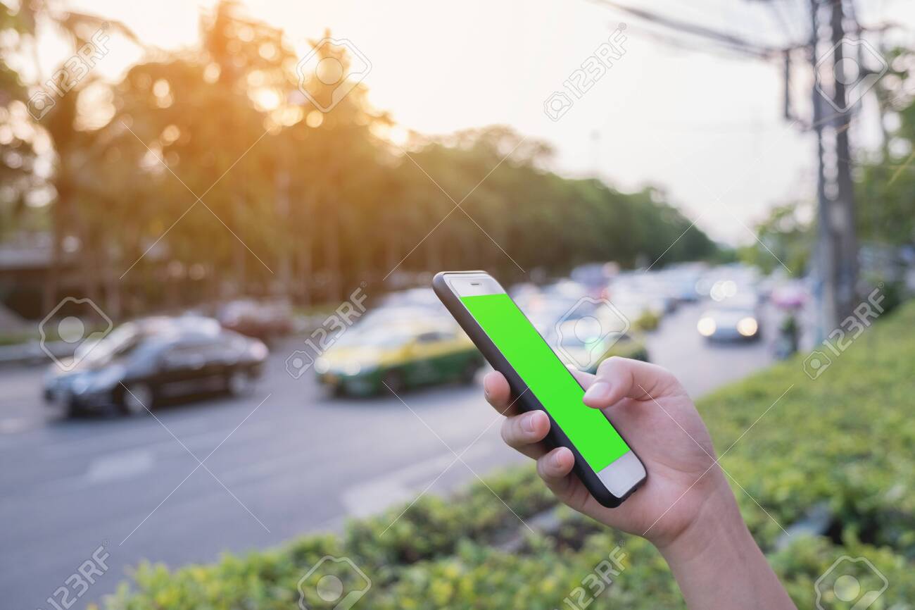 Hand hold mobile phone with mock up green screen, traffic background, on sunset time, technology and outdoor - 122663451 Hand hold mobile phone with mock up green screen, traffic background, on sunset time, technology and outdoor - 122663451