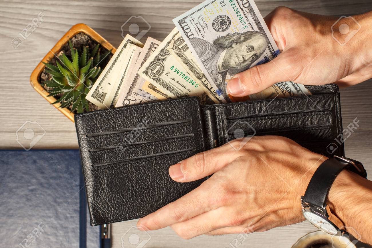 Las Manos Del Hombre Que Sostienen La Cartera De Cuero Negra Llena De Billetes De Dólar Fondo Gris. Vista Superior Fotos, Retratos, Imágenes Y Fotografía De Archivo Libres De Derecho. Image